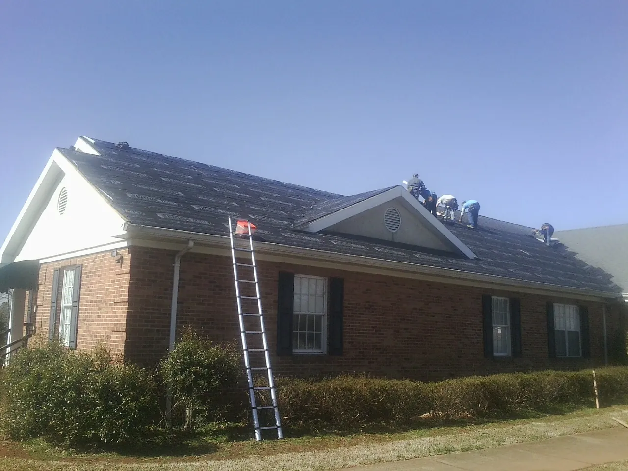 Crew tearing shingles off a brick ranch roof with a ladder set — Metal Roof Repair work by our crew in Holland